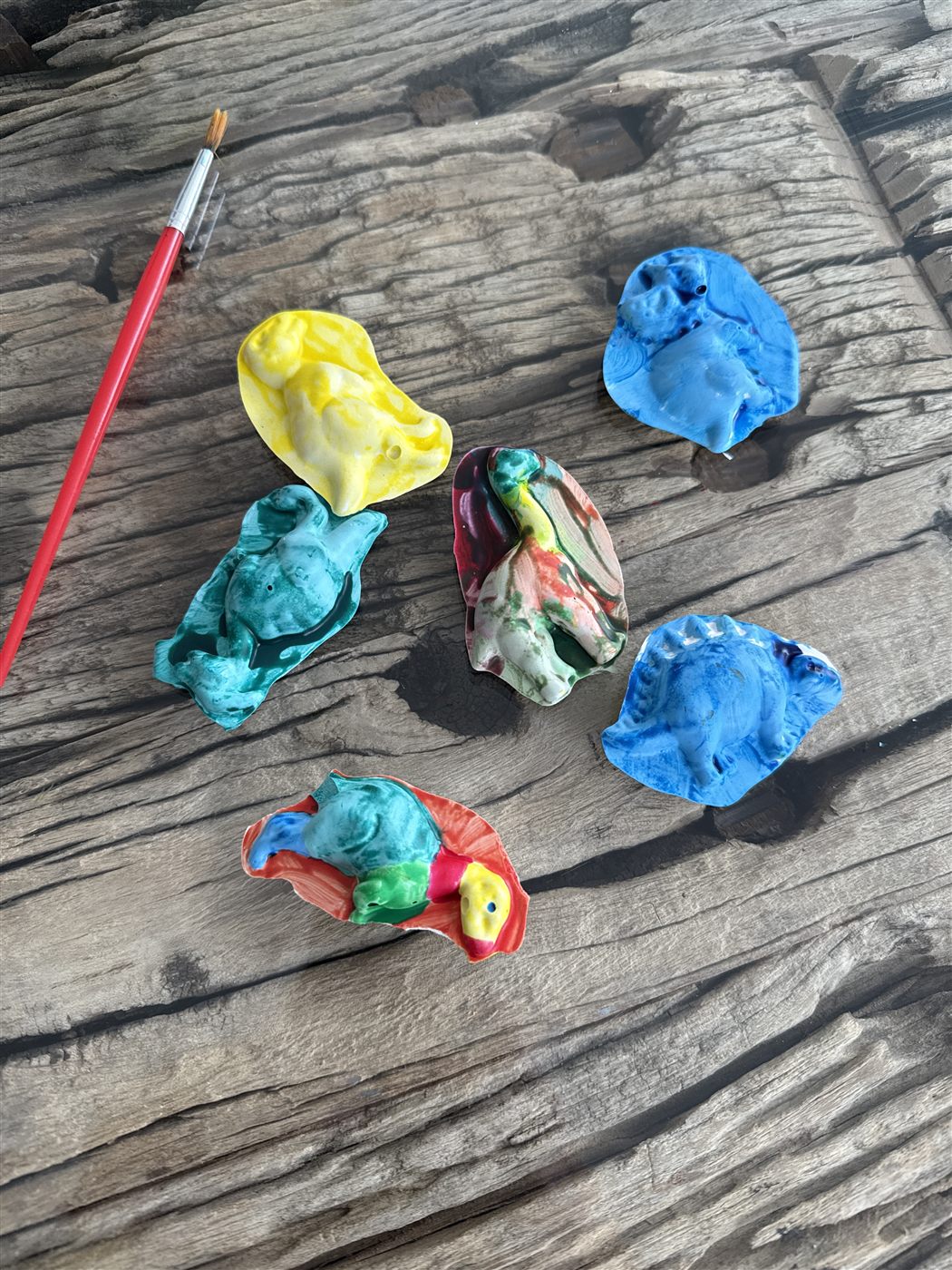 Six painted clay birds drying on weathered wood